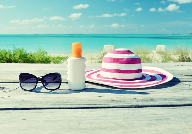 Sun hat, sun glasses and sun lotion on a table overlooking a beach