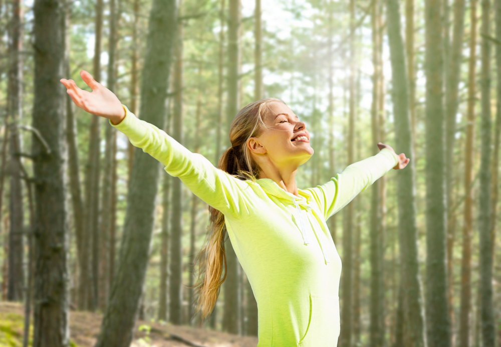 Happy woman in the woods with arms stretched out