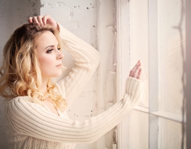 Close up of woman looking lout of a window whilst feeling sad