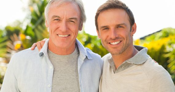 A middle-aged man and grown up son smiling