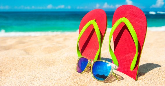 Flip floops and sunglasses on a beach with the sea in the background representing summer holidays