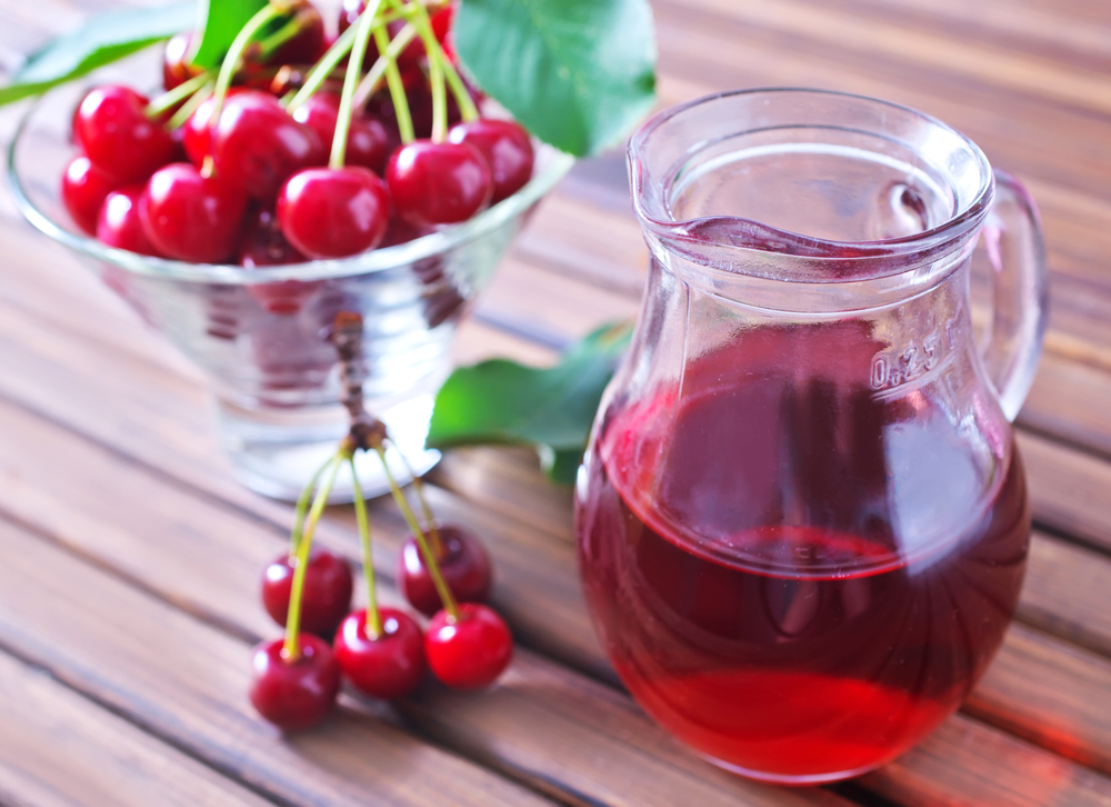 A bunch of cherries and a jug of cherry juice on a wooden table