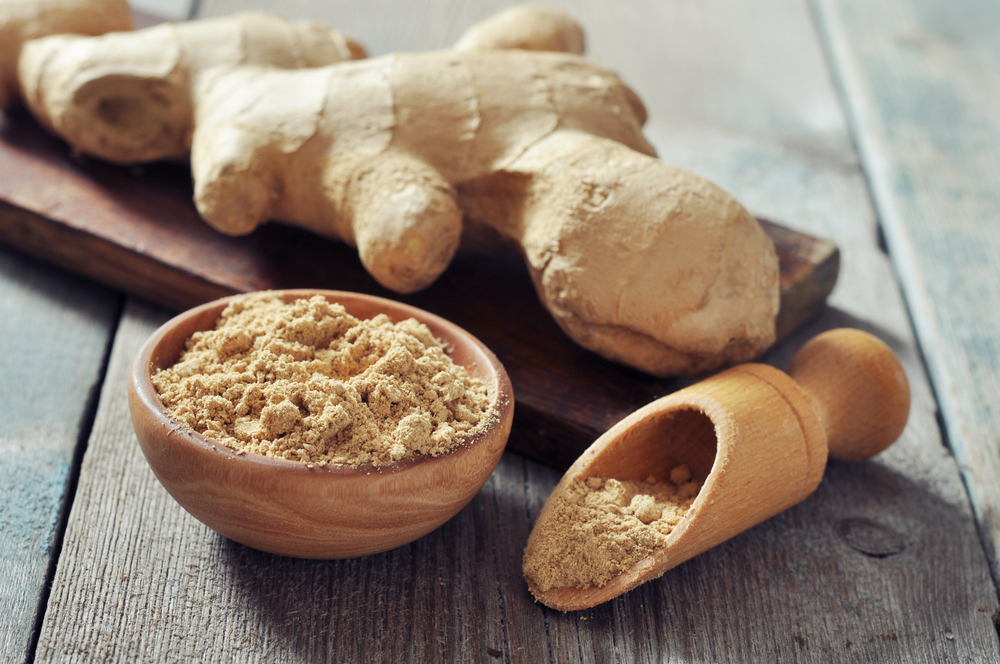 Ginger root and groud ginger spice in wooden pot