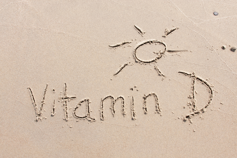 The words 'Vitamin D' and a picture of a sunshine written in the sand on a beach