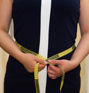 Woman using a measuring tape to measure her waist