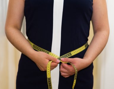 Woman using a measuring tape to measure her waist