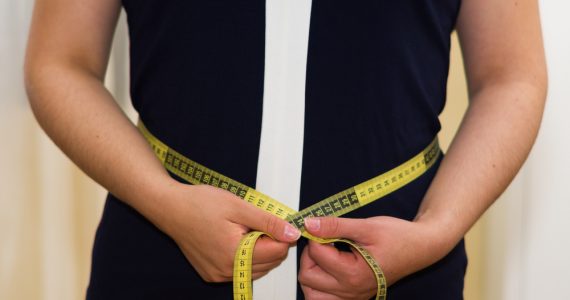 Woman using a measuring tape to measure her waist