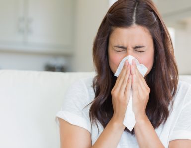 Close up of woman with a cold blowing her nose with a tissue.