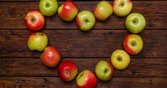 Red and green apples arranged in a heart shape on a wooden background