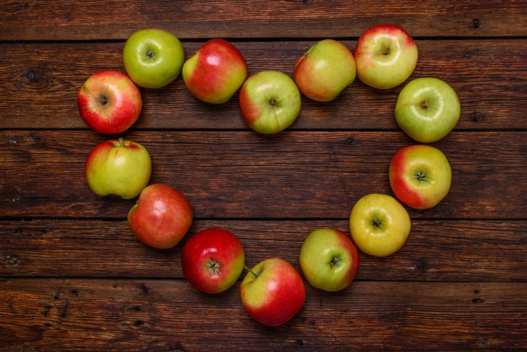 Red and green apples arranged in a heart shape on a wooden background