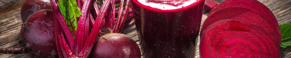 Whole and sliced beetroot surrounding a glass of beetroot juice