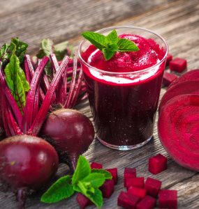 Whole and sliced beetroot surrounding a glass of beetroot juice
