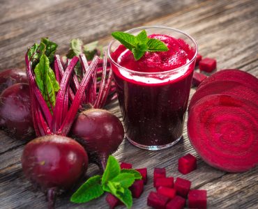 Whole and sliced beetroot surrounding a glass of beetroot juice