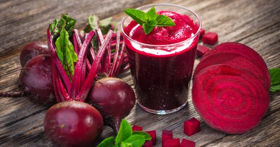 Whole and sliced beetroot surrounding a glass of beetroot juice