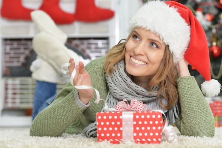 Happy woman wearing Christmas hat, relaxing on the floor with a present