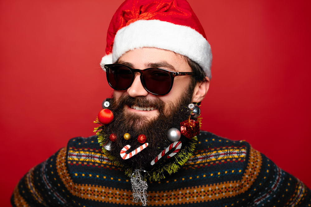Man in Christmas hat and sunglassed with beard decorated with Christmas decorations