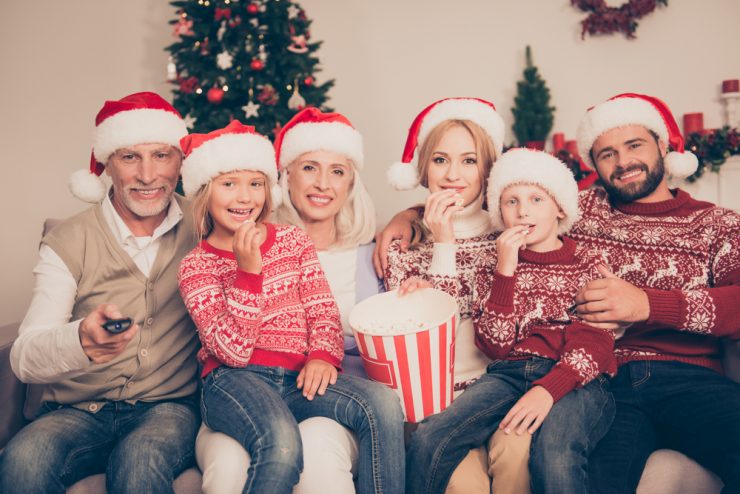 Multi-generational family wearing Christmas hats sitting on a sofa smiling