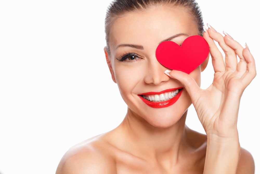 Headshot of woman holding a red paper heart over one eye