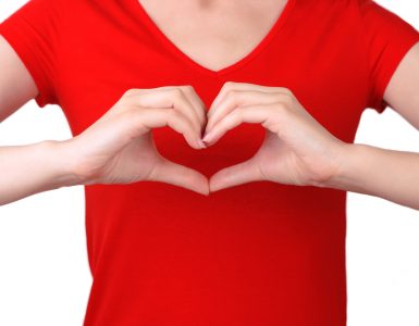 Torso shot of woman in red t-shirt making a heart symbol with her hands in front of her chest