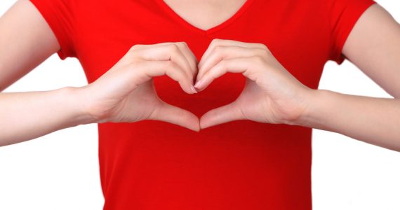 Torso shot of woman in red t-shirt making a heart symbol with her hands in front of her chest