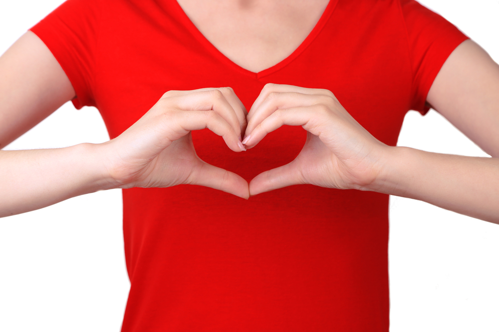 Torso shot of woman in red t-shirt making a heart symbol with her hands in front of her chest