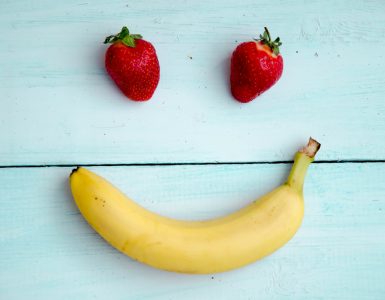 two strawberries and a banana made to look like a happy face on a blue wooden background