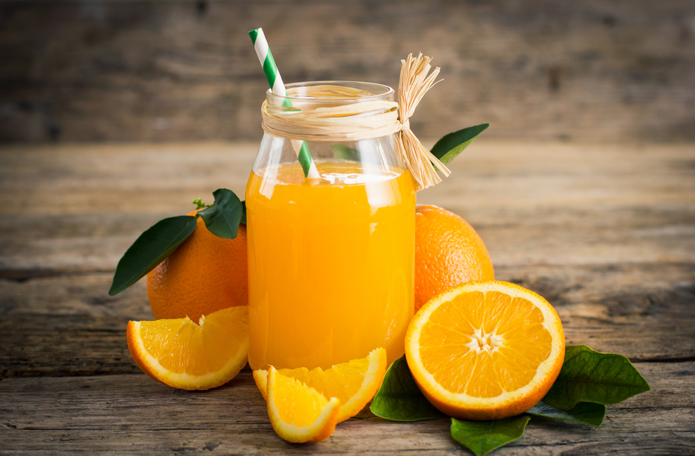A jam jar filled with orange juice surrounded by cut-up oranges