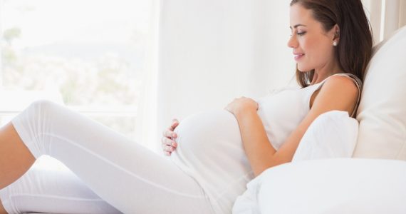 Pregnancy shown by image of pregnant woman lying on bed smiling and cradling her stomach