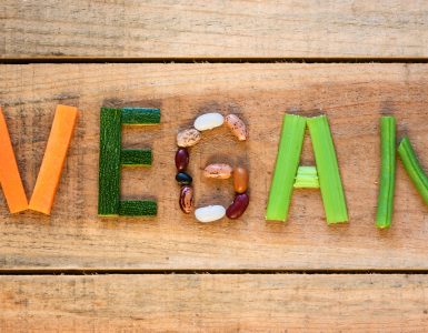 Vegetables laid out on wooden background to spell the word vegan