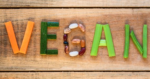 Vegetables laid out on wooden background to spell the word vegan