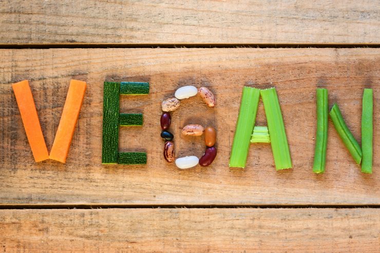 Vegetables laid out on wooden background to spell the word vegan