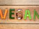 Vegetables laid out on wooden background to spell the word vegan