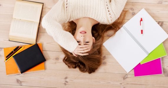 Woman lying on floor surrounded by work representing stress