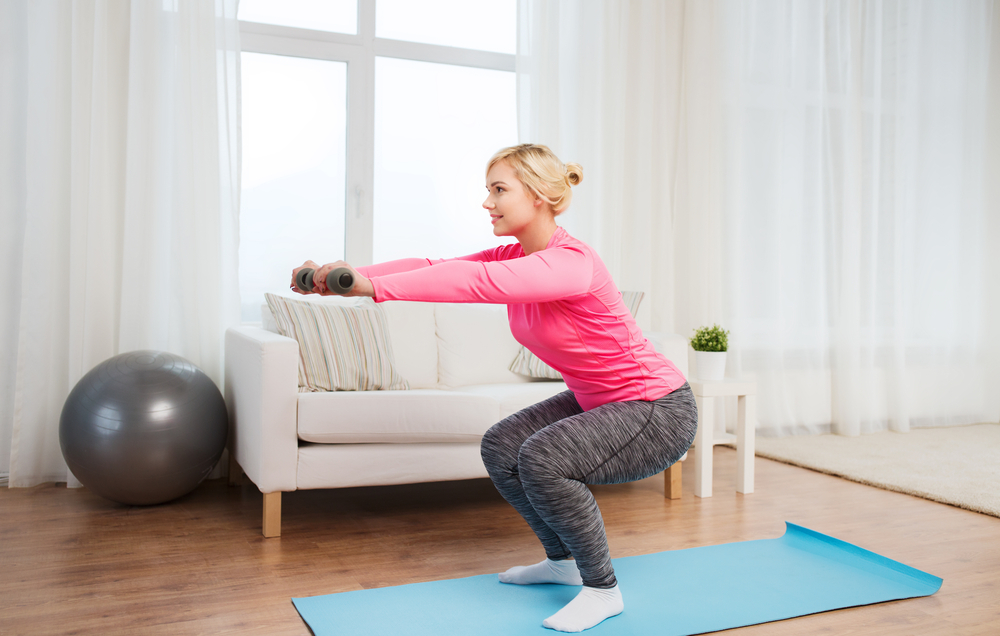 Woman squatting with weights in her lounge to show working out at home