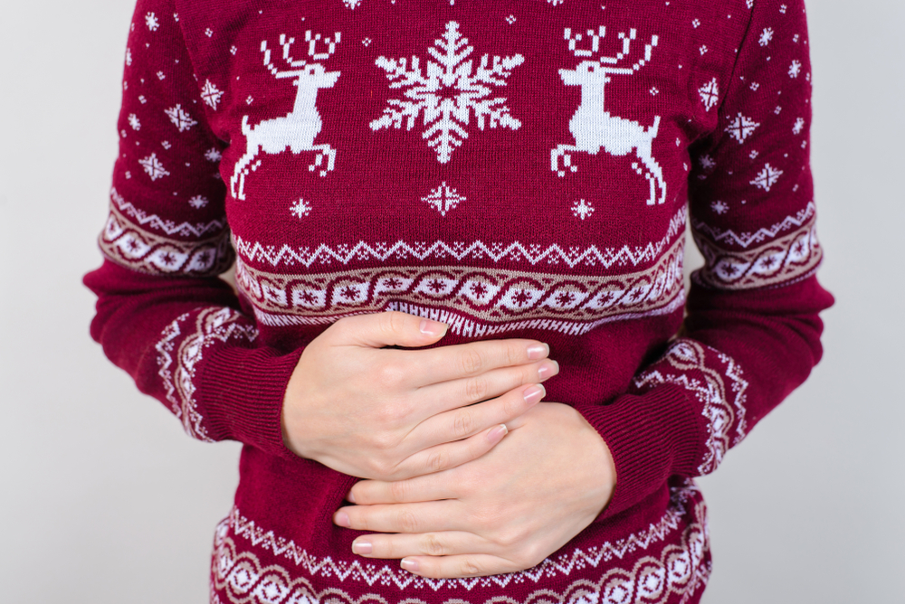Close up on woman with hands on tummy wearing a christmas jumper to represent indigestion