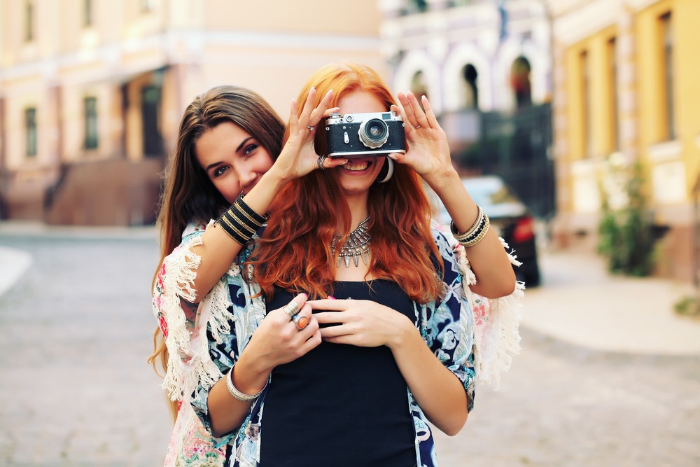 Two friends having fun with one holding up a camera in front of the other one's face so she can see the view