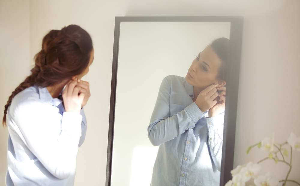 Woman drssed putting earring in in front of mirror