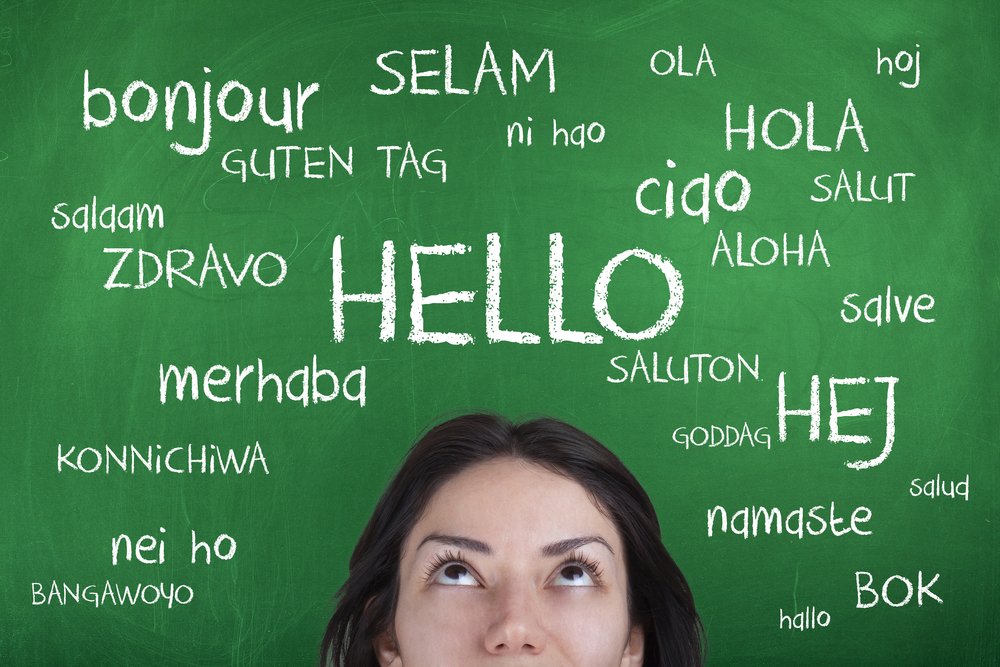 Close up of woman with the word 'hello' in many languages on a blackboard behind her to represent learning a new language