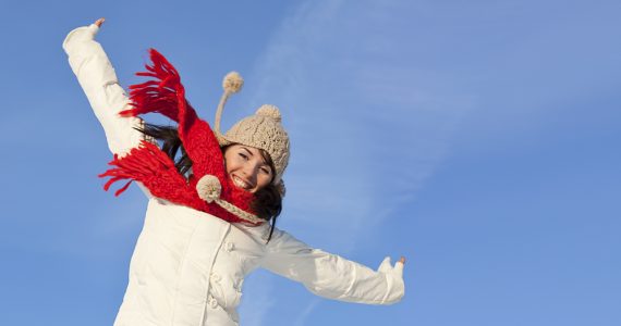 Woman in hat and scarf jumping wiht energy outdoors
