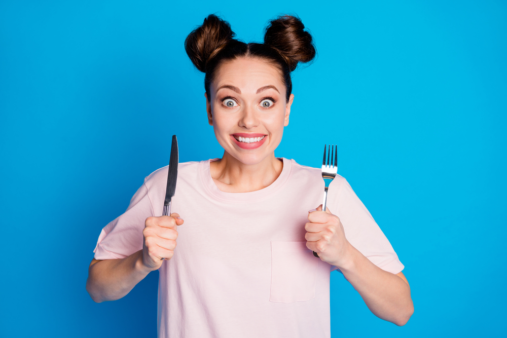 Woman holding knifeand fork to represent feeling hungry